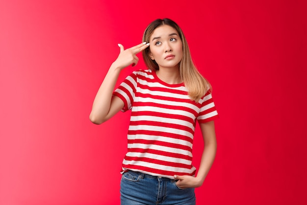 Upset blond asian girl wear striped tshirt jeans dying boredom sighing look up hold finger gun pisto...