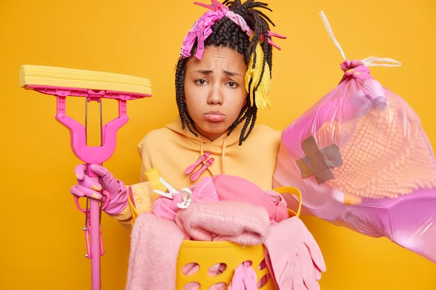 Free photo upset bored young african american woman with dreadlocks collects rubbish in trash bag