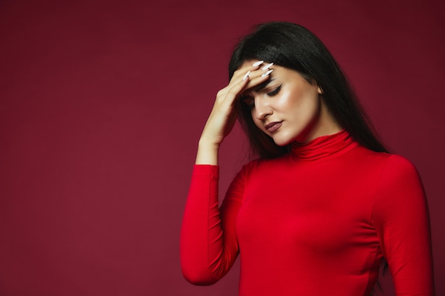 Free photo upset brunette caucasian girl dressed in red pullover with annoying headache put hand on the forehead