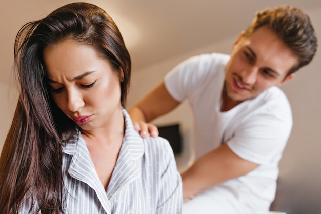 Upset brunette woman in pajama looking down while husband talk to her