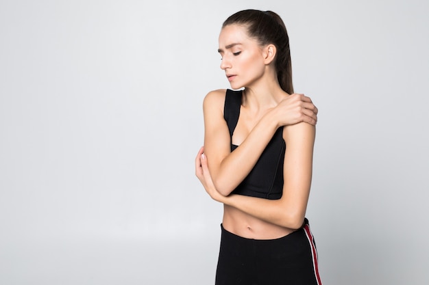 Upset brunette young woman injured arm during sport training, touches her wrist isolated on white wall