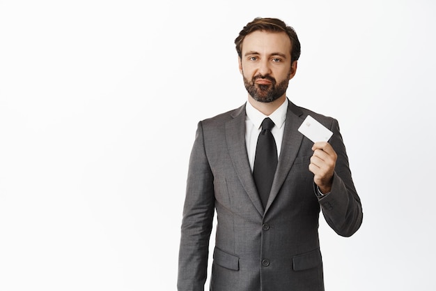 Расстроенный бизнесмен показывает кредитную карту и гримасничает, стоя на белом фоне
