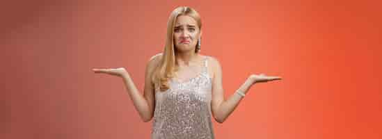 Free photo upset clueless frustrated blond european young girl in glittering silver evening dress grimacing