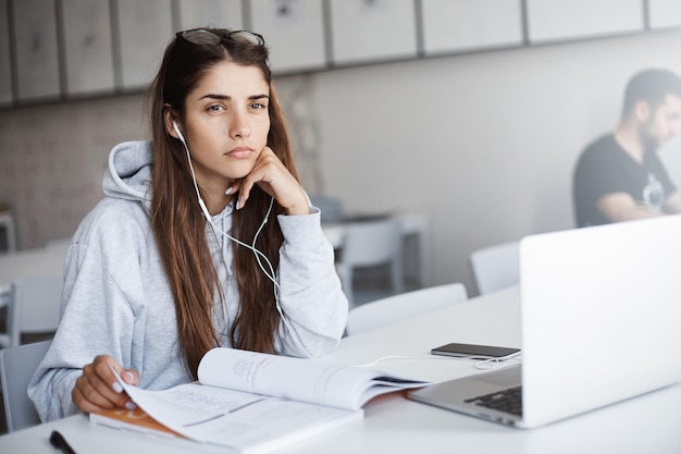 Upset and concentrated young caucasian female student with long dark hair reading a study book looking off camera with a grumpy face Education concept