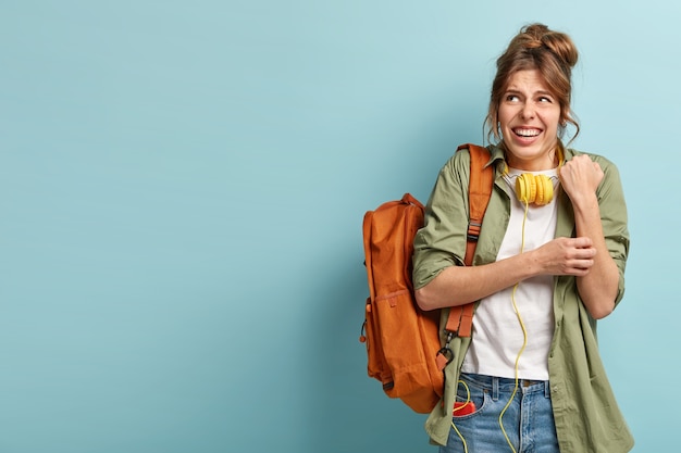 Upset displeased female rubs hand, looks upwards, smirks face in dissatisfaction, wears yellow headphones