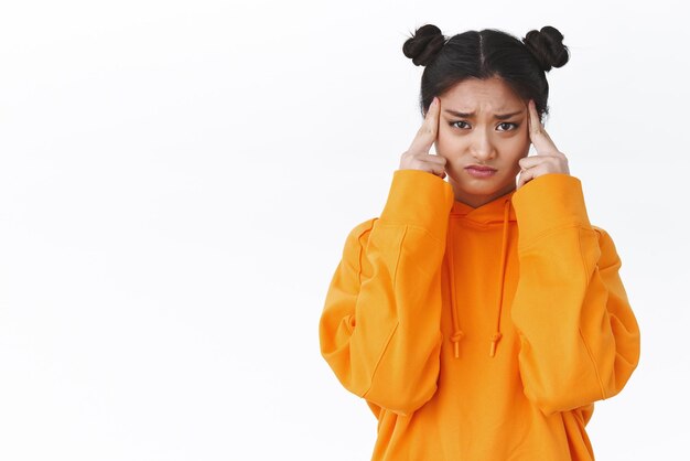 Upset and dizzy cute asian girl feel unwell got tired or sick massaging temples and frowning grimace looking camera suffer headache serious migraine standing white background uneasy cant think