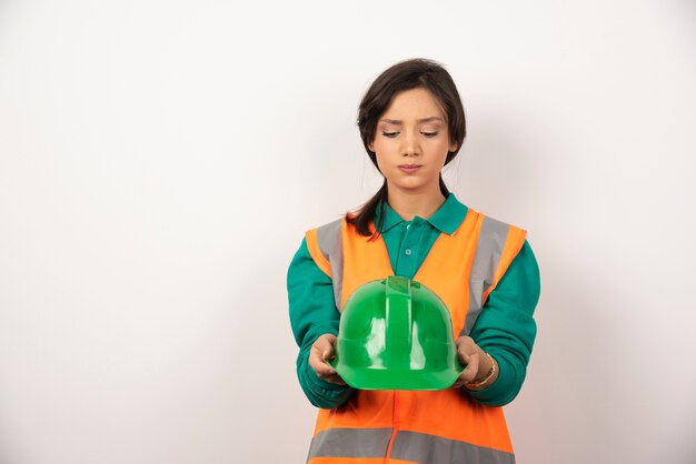 Upset female engineer holding a helmet on white background.