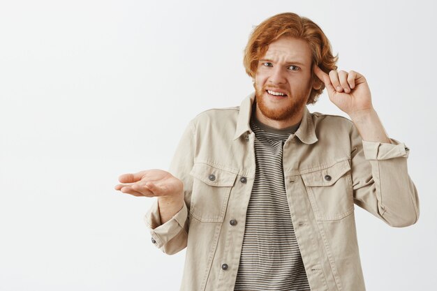 Upset and frustrated bearded redhead guy posing against the white wall
