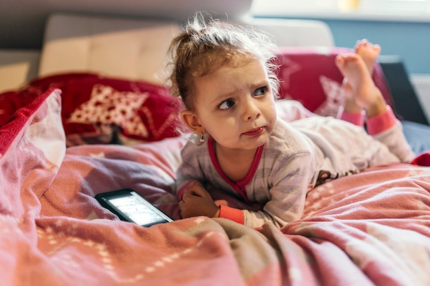 Upset girl with smartphone lying on bed