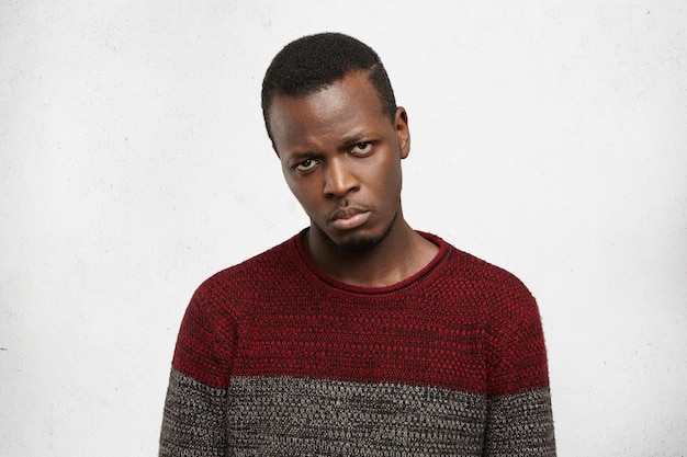 Free photo upset handsome young dark-skinned male dressed in casual sweater looking with disappointment and sadness, feeling unhappy and betrayed because his friends didn’t invite him to party