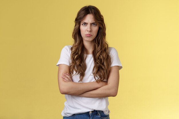 Upset jealous moody clingy girlfriend sulking offended cross hands chest blocking pose frowning disappointed complaining unfair treatment stand yellow background bothered pouting childish