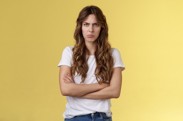 Upset jealous moody clingy girlfriend sulking offended cross hands chest blocking pose frowning disappointed complaining unfair treatment stand yellow background bothered pouting childish