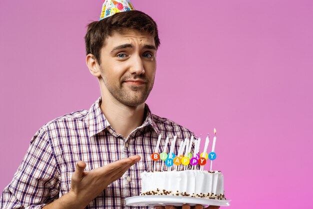 Upset man holding birthday cake with one not blow out candle.