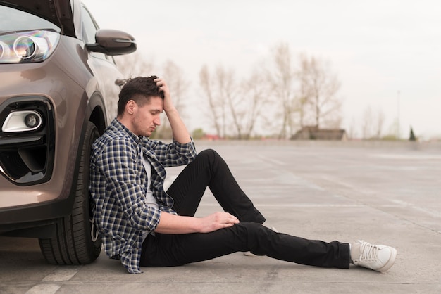 Free photo upset man sitting beside broken down car