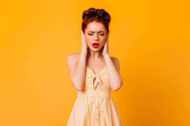 Upset pinup female model covering ears with hands. studio shot of attractive caucasian woman isolated on yellow space