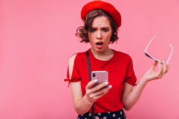 Upset short-haired girl reading phone message. Indoor photo of surprised french female model in beret posing with mouth open.