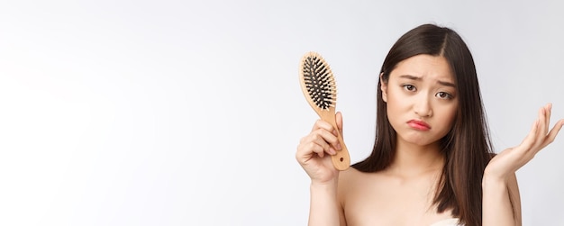 Upset stressed young Asian woman holding damaged dry hair on hands over white isolated background