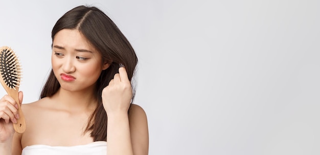 Upset stressed young Asian woman holding damaged dry hair on hands over white isolated background