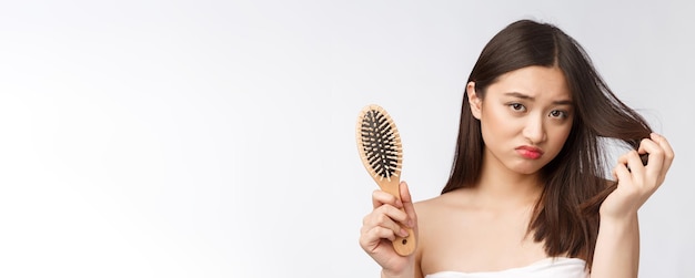 Upset stressed young Asian woman holding damaged dry hair on hands over white isolated background