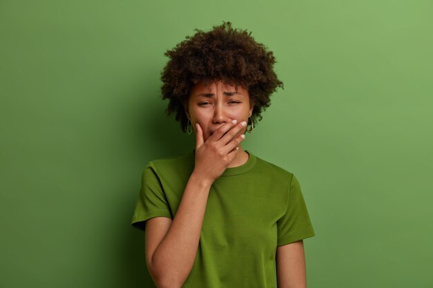 Upset stressful woman in despair, feels depressed, sobs or whins loudly, cannot stop crying, faces troublesome situation, stands grieved against vibrant green wall. Negative emotions concept