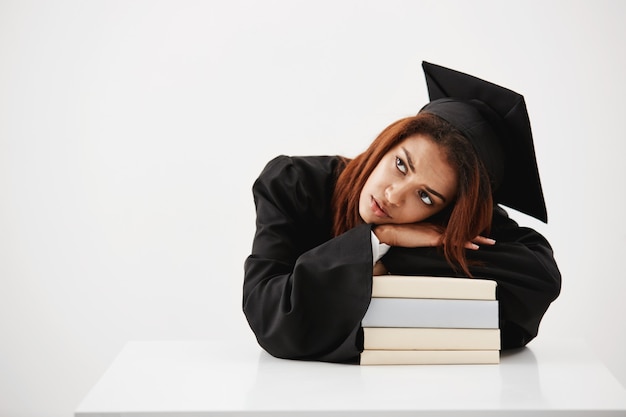 Upset and tired of studying african student woman and future graduate laying on books thinking about profession and diploma sitting. Copy space.