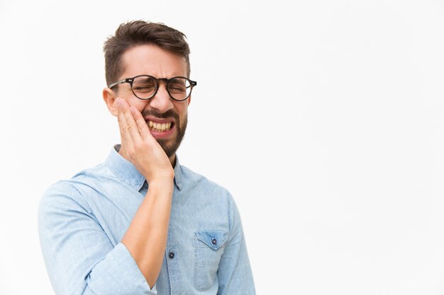 Upset unhappy guy holding cheek with pain face