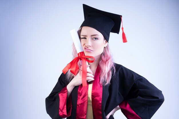 Upset woman in a bachelor cap and mantle holds her graduation certificate