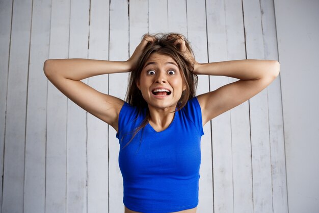 Free photo upset woman holding hair in hands over white wooden wall.