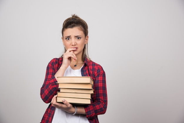 An upset woman holding a stack of books on a gray wall.