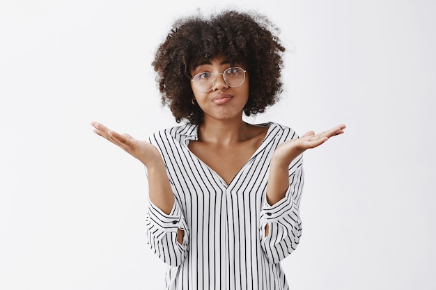 upset woman losing in battle shrugging with spread palms aside pursing lips and frowning from disappointment and regret being unhappy and gloomy after bad result over gray wall