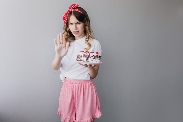 Upset woman in pink skirt posing with birthday cake. stylish girl with pie isolated.