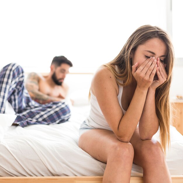Расстроенная женщина, сидящая на кровати перед мужем