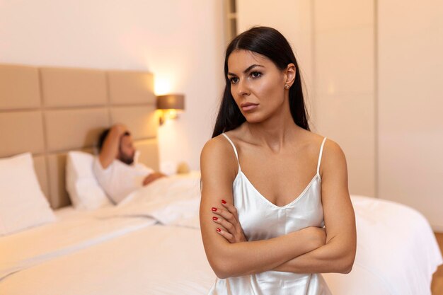 Расстроенная женщина сидит на кровати с мужчиной на заднем плане Женщина и мужчина ссорятся Молодая пара в постели скучает женщина