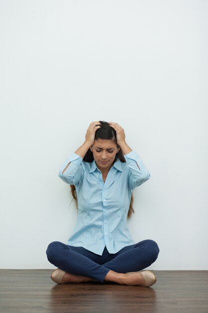 Upset Woman Sitting on Floor and Clutching Head