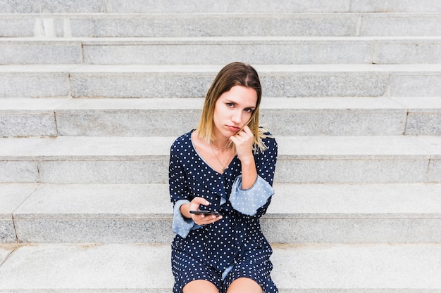 Upset woman sitting on staircase holding cellphone