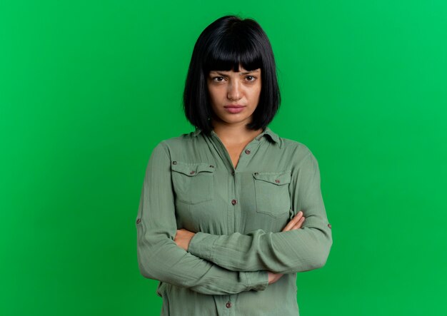 Upset young brunette caucasian girl stands with crossed arms isolated on green background with copy space