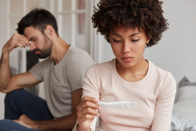 Расстроенная молодая пара позирует дома с тестом на беременность