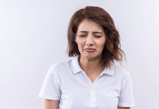 Upset young girl with short hair wearing white polo shirt looking cryring with sad expression on face 