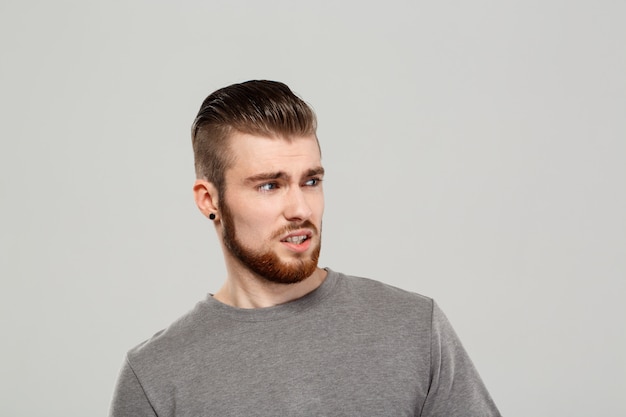 Upset young handsome man posing over grey wall.