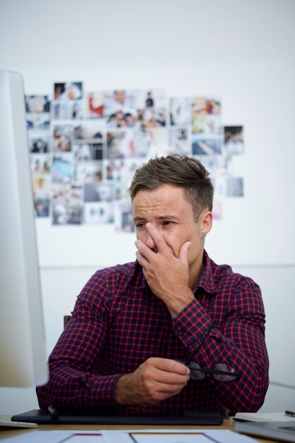 Upset young man looking at computer screen, covering face with hand and crying