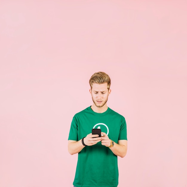 Расстроенный молодой человек, используя мобильный телефон на розовом фоне