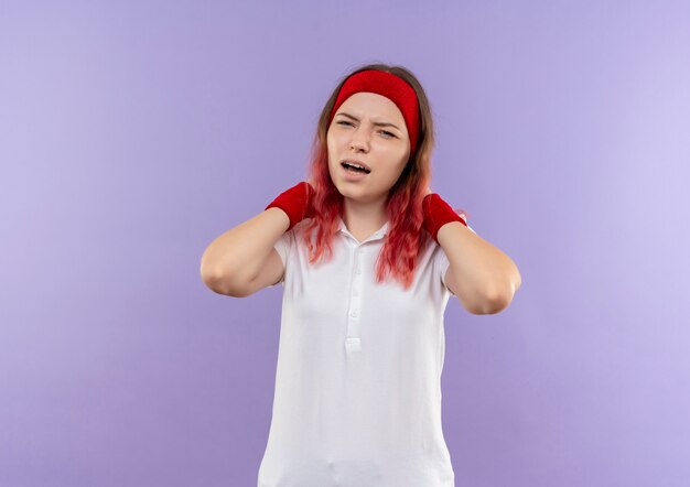 Расстроенная молодая спортивная женщина с раздраженным выражением лица стоит над фиолетовой стеной