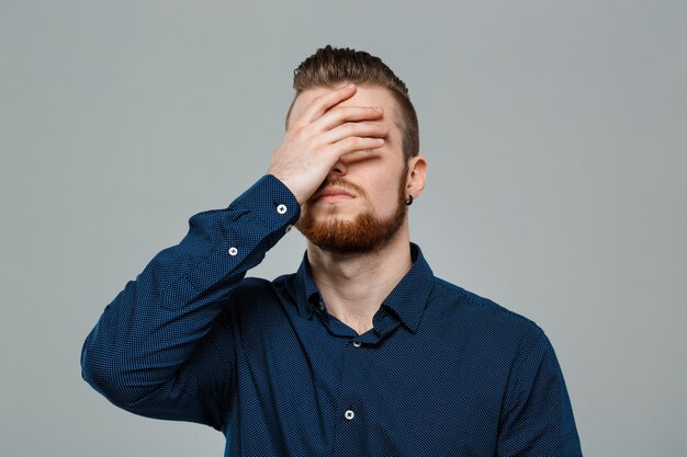 Upset young successful businessman posing over grey wall.