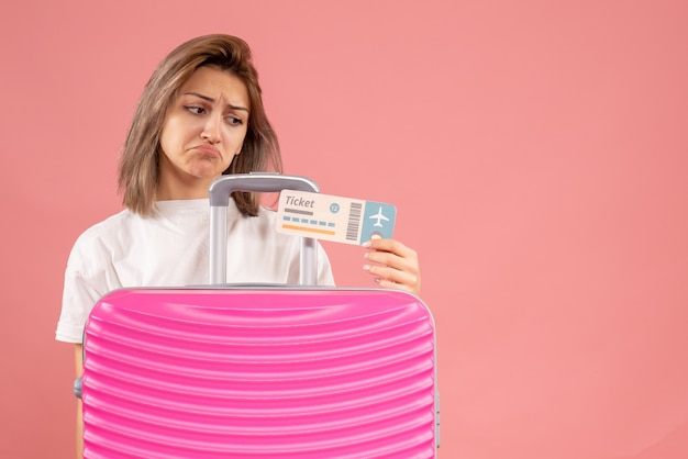 Расстроенная молодая женщина с розовым чемоданом смотрит на билет