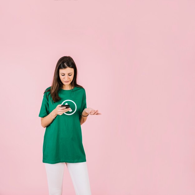 upset young woman with smartphone shrugging against pink background
