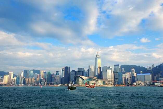 青い空、ボート、雲のある日の香港ビクトリアハーバーの都市建築。