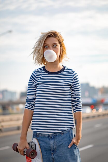 Urban stylish young girl walking with skateboard. Outdoors portrait of active sport woman model. Healthy lifestyle. Extreme sports. Fashion look, outdoor hipster portrait. Close up portrait of a prett