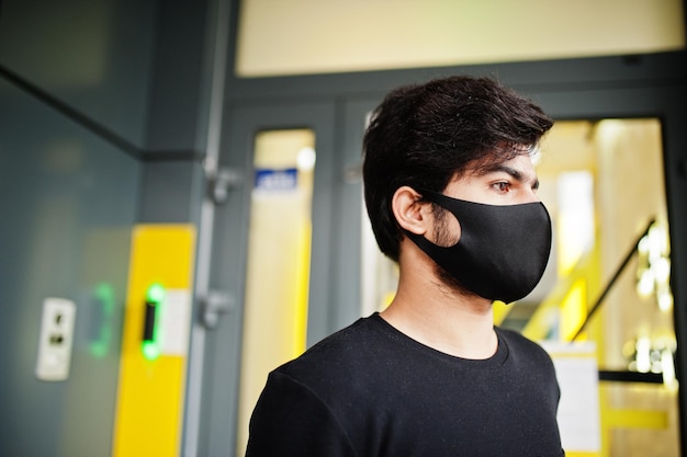 Free photo urban young hipster indian man wear all black stand near code entrance cool south asian guy with face protect mask during new normal