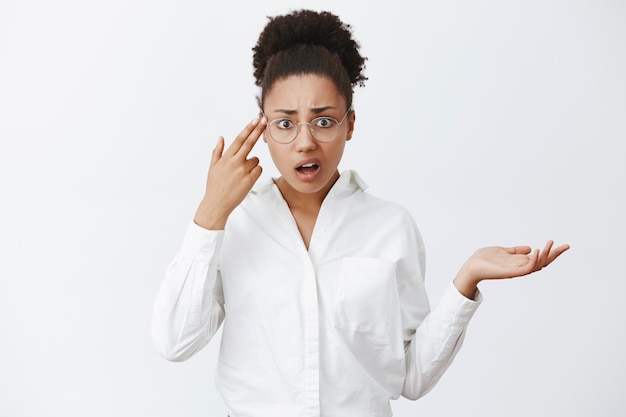 Use your brain, stupid. Annoyed and displeased good-looking african-american entrepreneur in glasses and white shirt, shrugging and holding fingers on temple, looking at crazy or insane man