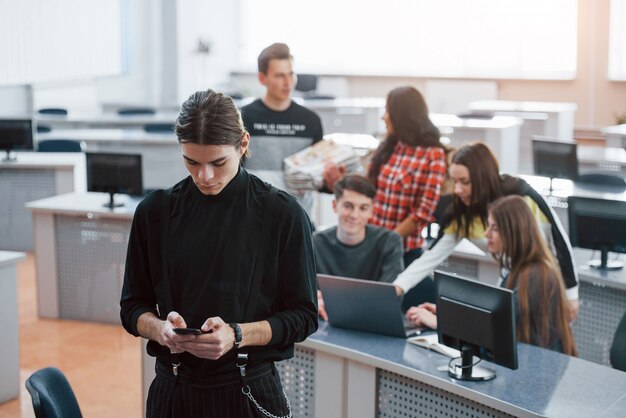 Using black colored smartphone. Group of young people in casual clothes working in the modern office